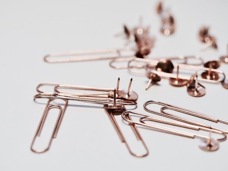 Aesthetic rose gold paperclips and thumb tacks on a white background, ideal for office decor or supplies imagery.