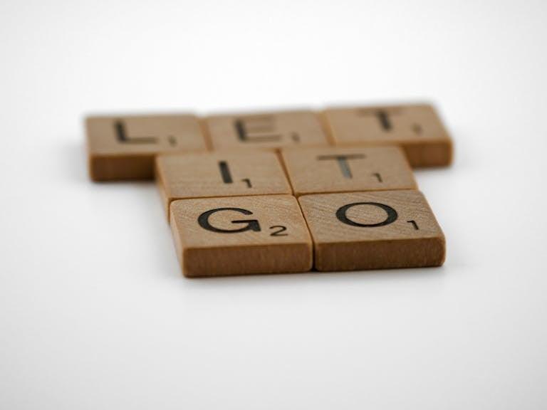 Close-up of wooden Scrabble tiles spelling 'Let It Go' on a white surface.